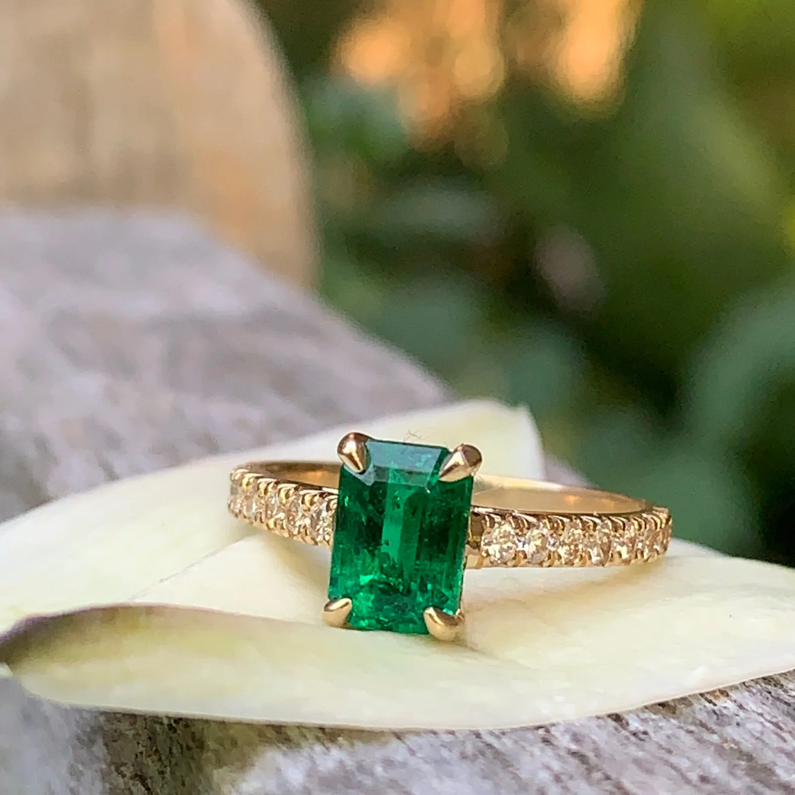 An emerald-cut emerald ring with a diamond band in warm evening light