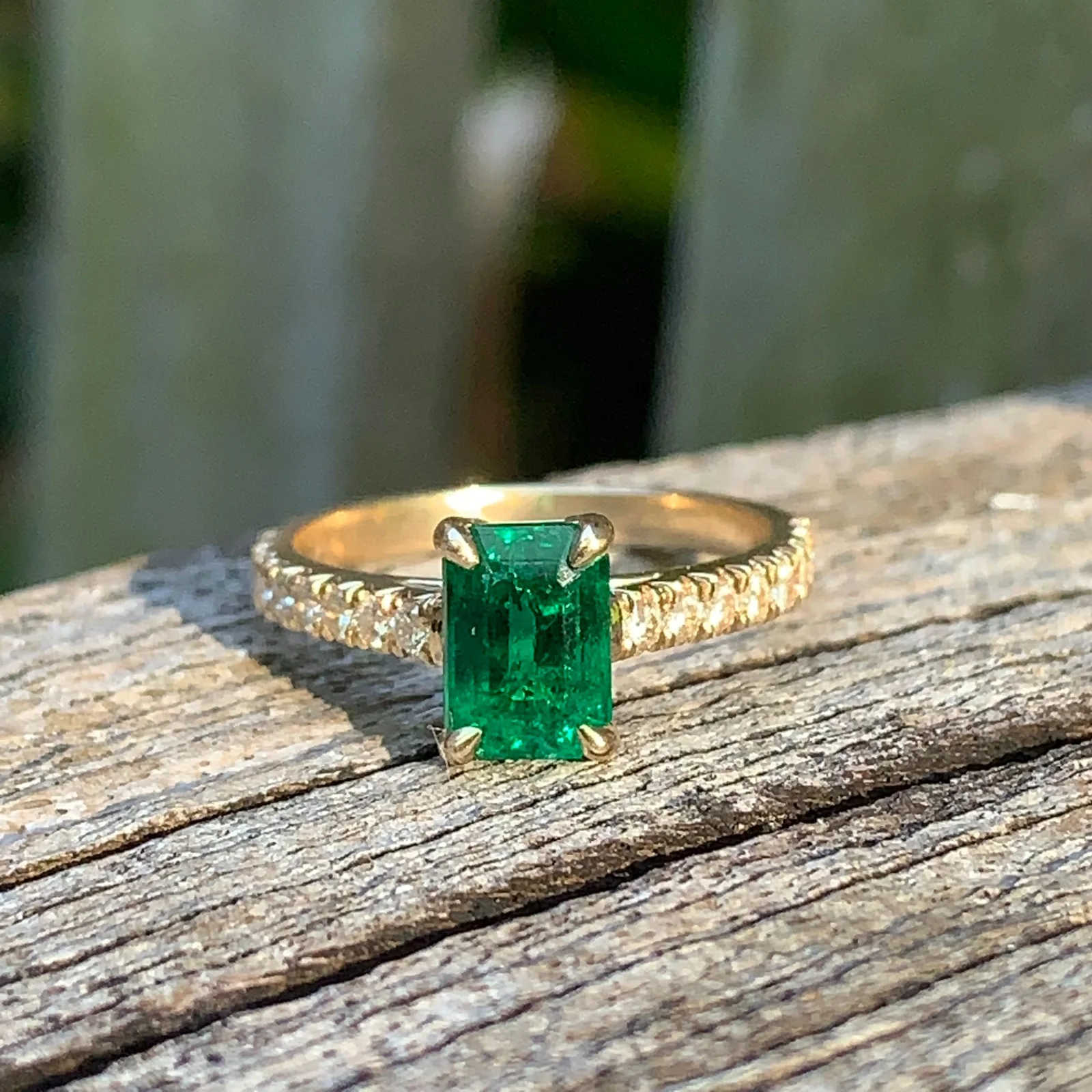 Emerald ring with a diamond band on weathered wood