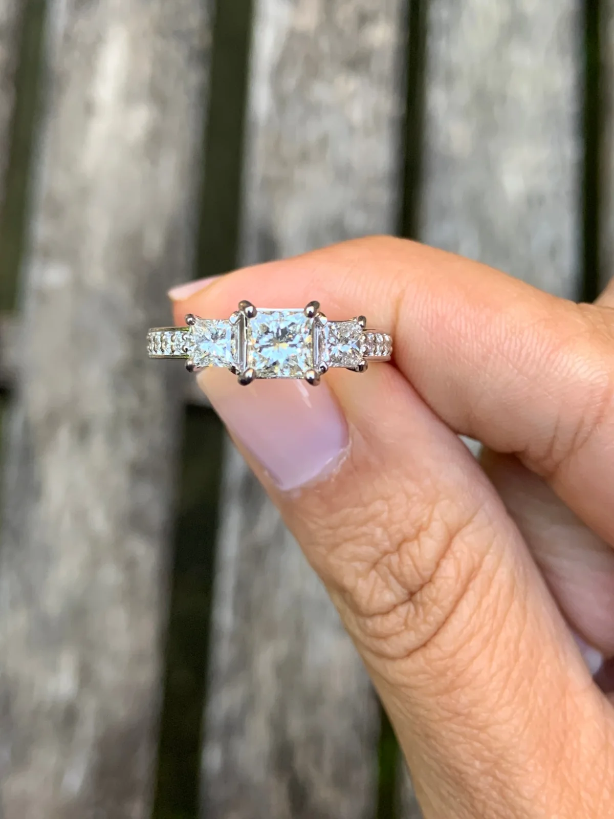 Princess-cut three-stone ring held between two fingers